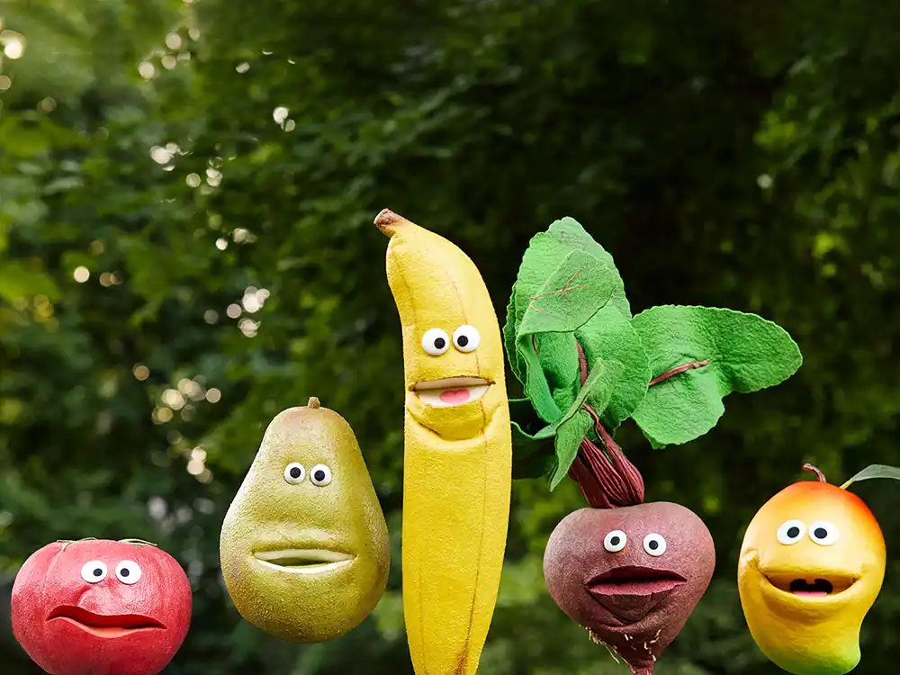 Tomato, pear, banana, beet, and mango puppets line up against leafy green, from Compleat x Elmo's What Is Better Than How