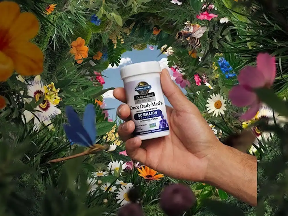 A hand holds Garden of Life Once Daily Men's probiotics in a wreath of flowers, from Formulas for Feeling Alive