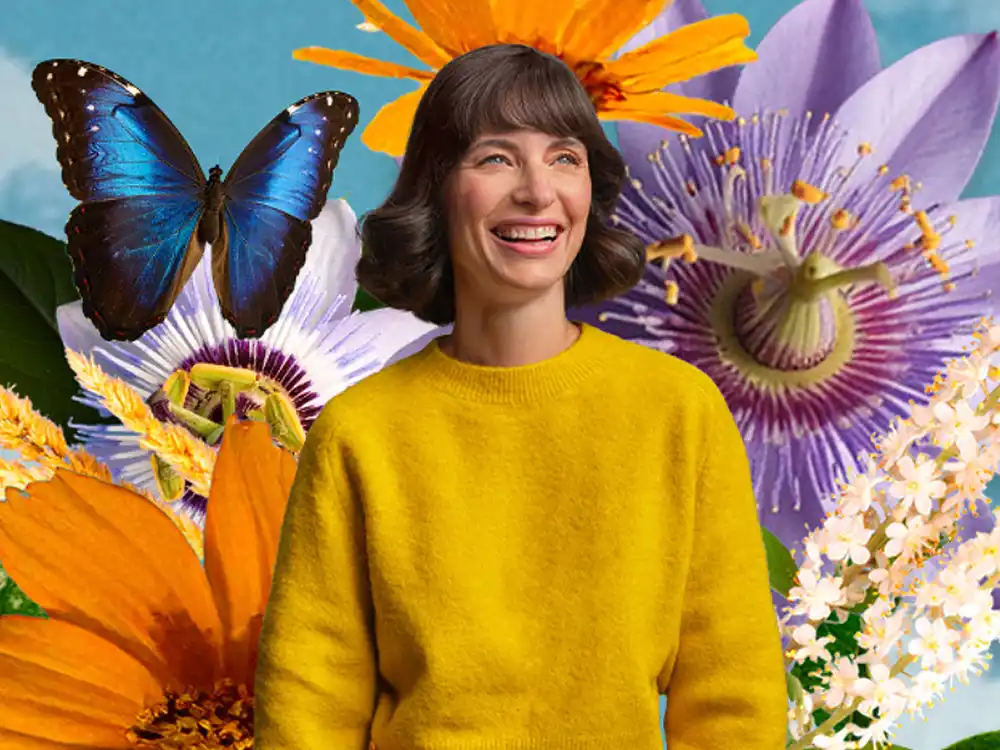 A laughing woman in a yellow sweater stands among passion flowers and a blue morpho, from Garden of Life's Formulas for Feeling Alive
