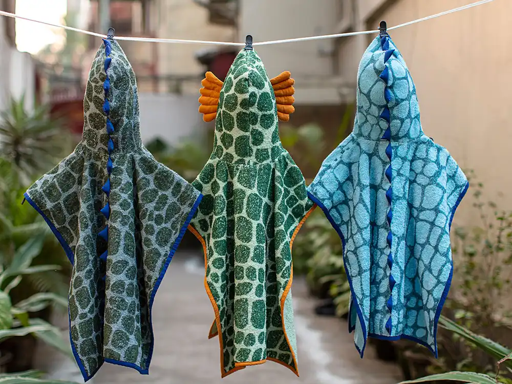 Three dinosaur-print hooded towels hang on a clothesline, from Jurassic World's Preserving Legacies of the Past collection