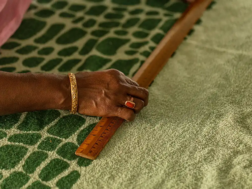 Hand with a gold bracelet measures scale-print terry with a wooden ruler, from Jurassic World's Preserving Legacies of the Past collection