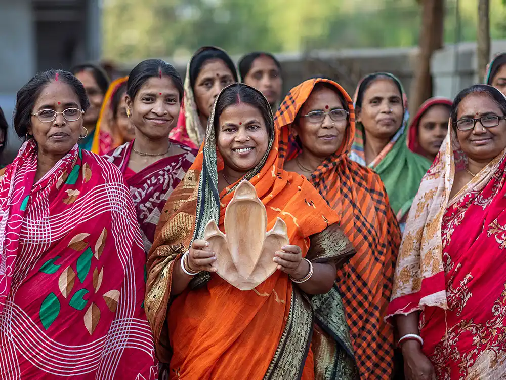 Woman in an orange sari holds a wooden dinosaur-footprint tray among a group, from Jurassic World's Preserving Legacies of the Past collection