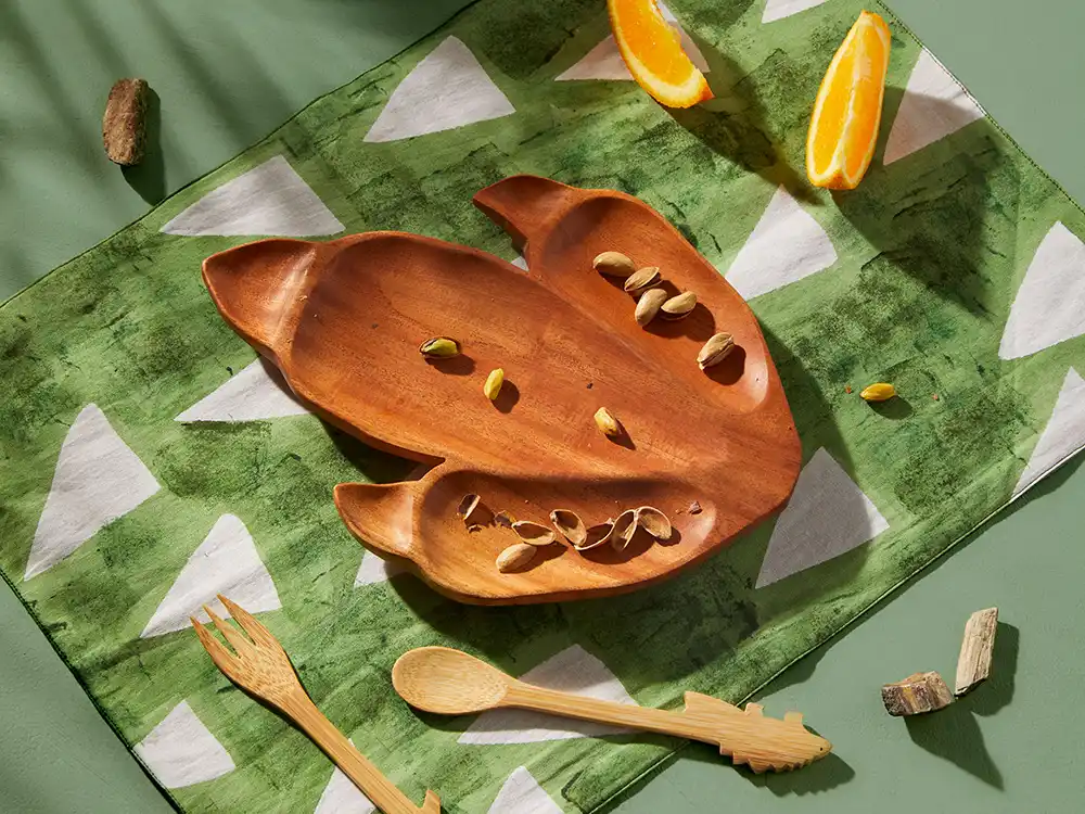 Wooden dinosaur-footprint serving tray with pistachios on a green patterned cloth, from Jurassic World's Preserving Legacies of the Past collection