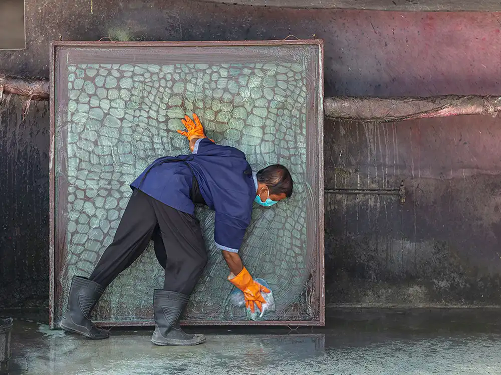 Worker in orange gloves presses a scale-pattern screen in a dye workshop, from Jurassic World's Preserving Legacies of the Past collection