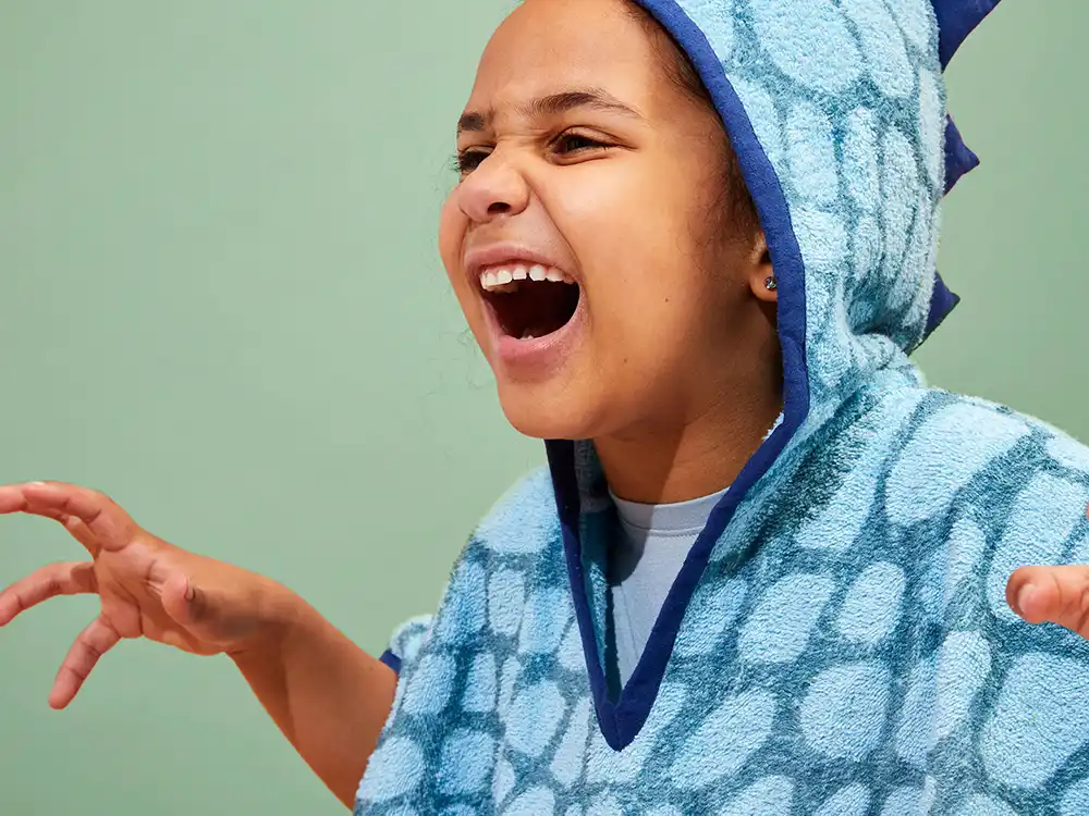 Child in a blue dinosaur hooded towel roars with arms outstretched, from Jurassic World's Preserving Legacies of the Past collection