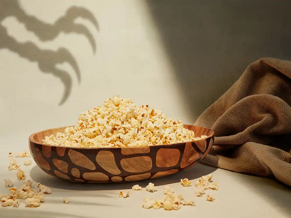 Wooden scale-pattern bowl of popcorn beside a claw shadow, from Jurassic World's Preserving Legacies of the Past collection