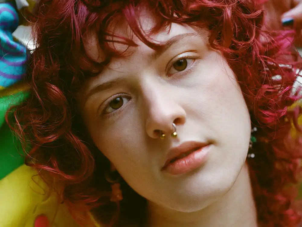 Close-up of a person with curly magenta hair, a septum piercing, and brown eyes, from Lambda Legal's All Rise campaign