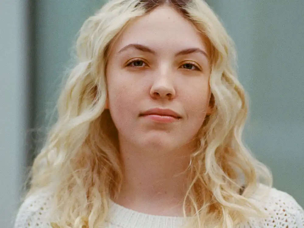 Close-up of a person with long wavy blonde hair in a white knit sweater, from Lambda Legal's All Rise campaign