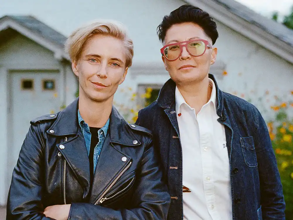 Two people in leather and denim jackets stand together before a white house, from Lambda Legal's All Rise campaign