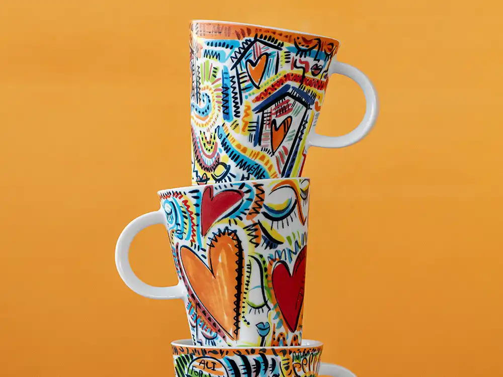 Three stacked white mugs painted with hearts, faces, and doodles against orange, from Nespresso's Innovation You Can Taste