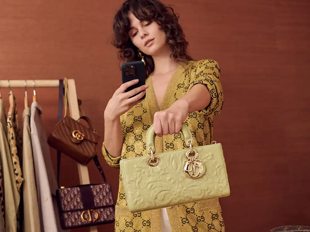 Woman in a gold monogram cardigan photographs a mint Dior tote, from Vestiaire Collective's Parlez-vous?
