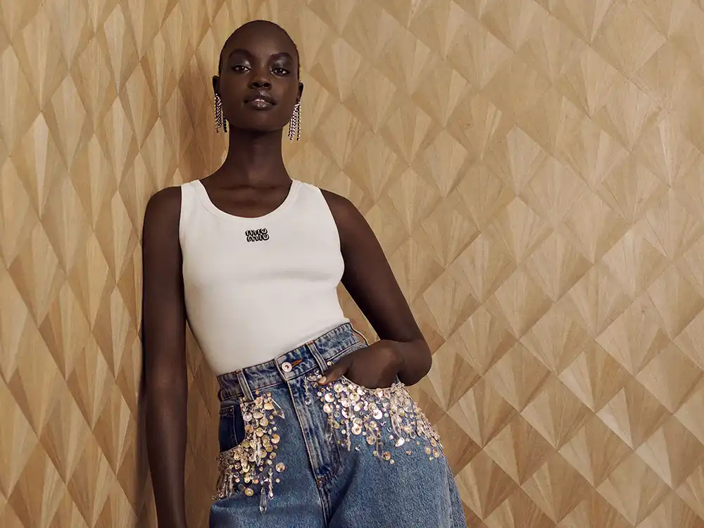 Woman in a white tank and sequin-embellished jeans leans on a geometric wood wall, from Vestiaire Collective's Parlez-vous?