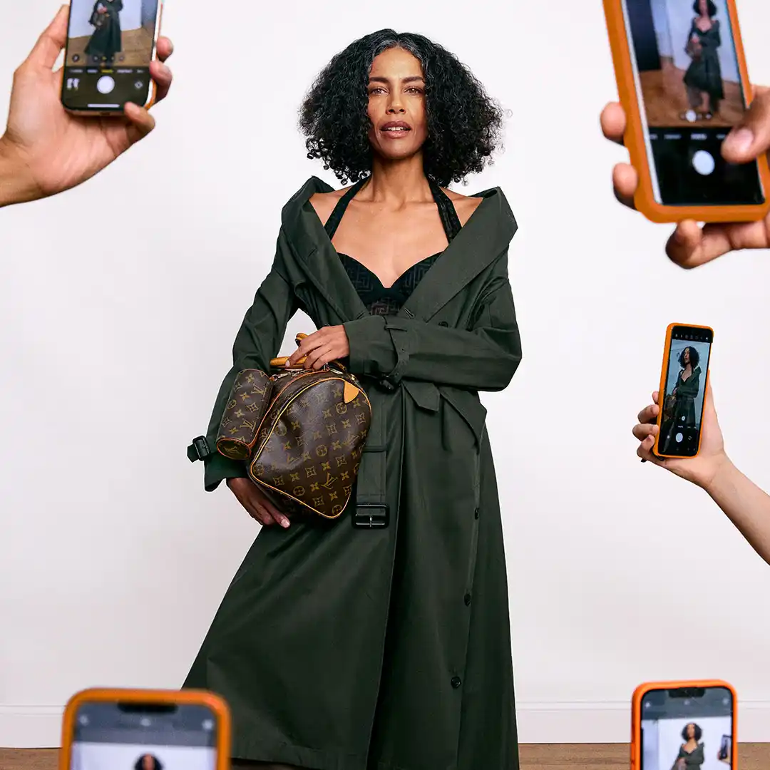 Woman in a green trench and monogram duffel poses while phones around her capture the look