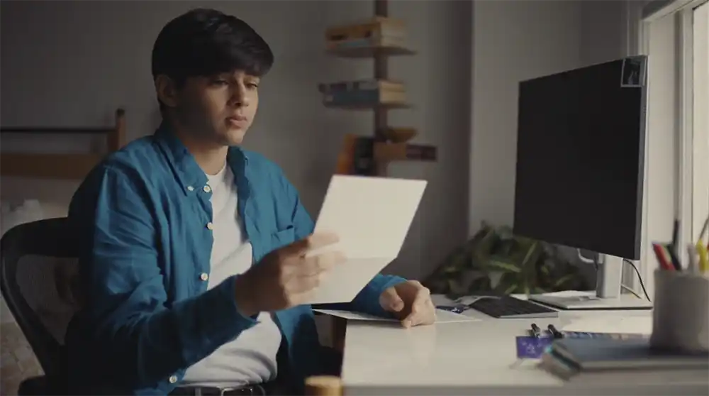 Sonu, a trans teenager in a blue shirt, reads a letter at his desk in Lambda Legal's Letters of Love film for The Advocate