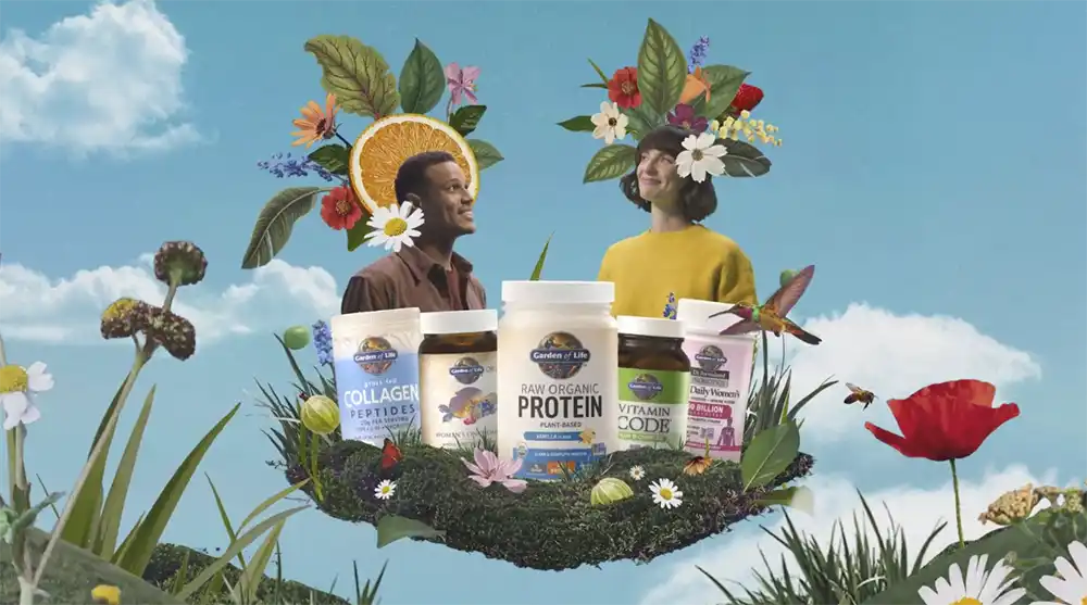 Garden of Life bottles sit on a moss island with two people crowned in flowers, from Formulas for Feeling Alive in The Drum