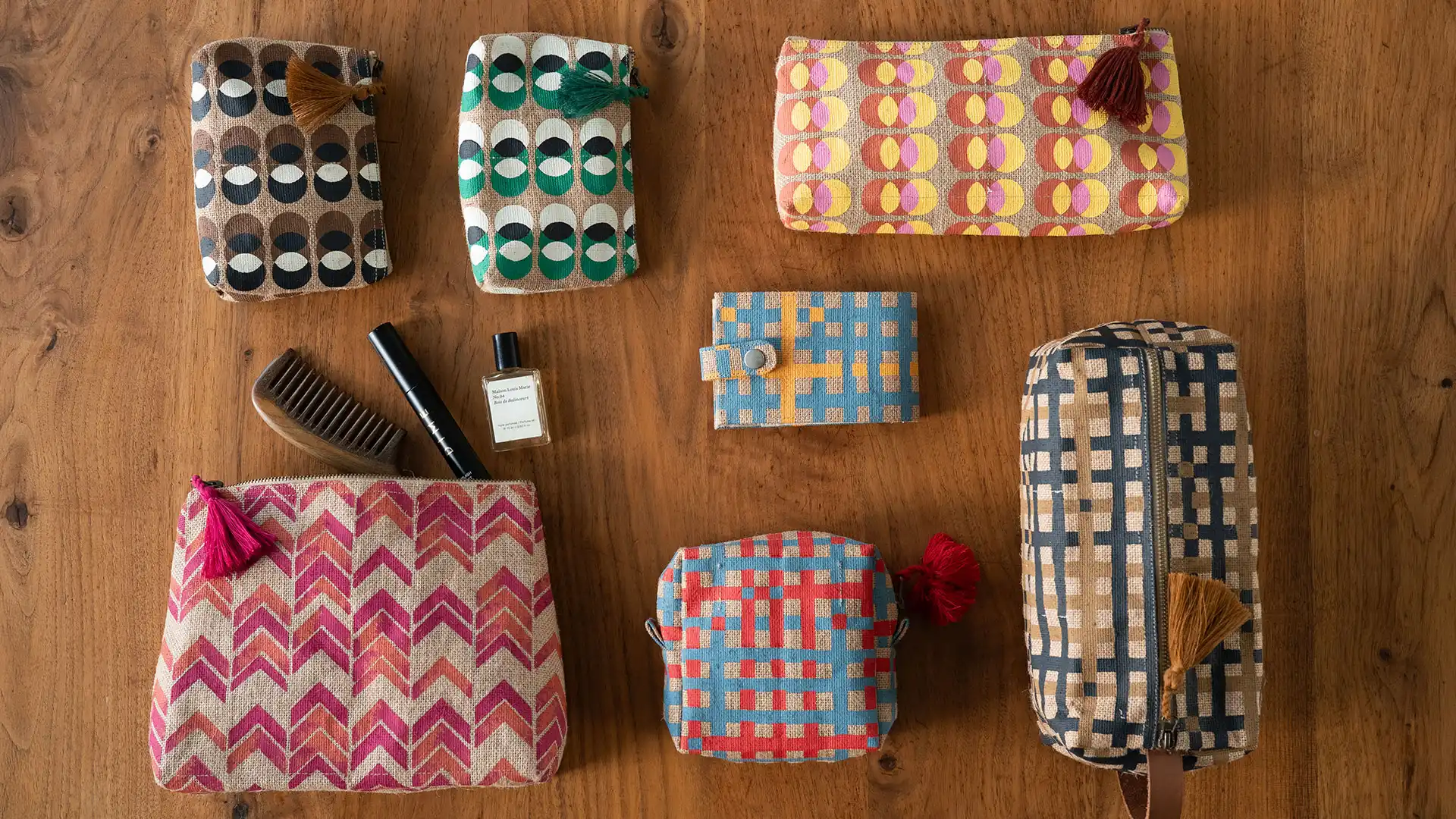 Patterned pouches, a comb, and a perfume bottle arranged on a wood table for WARC's gift-with-purpose feature